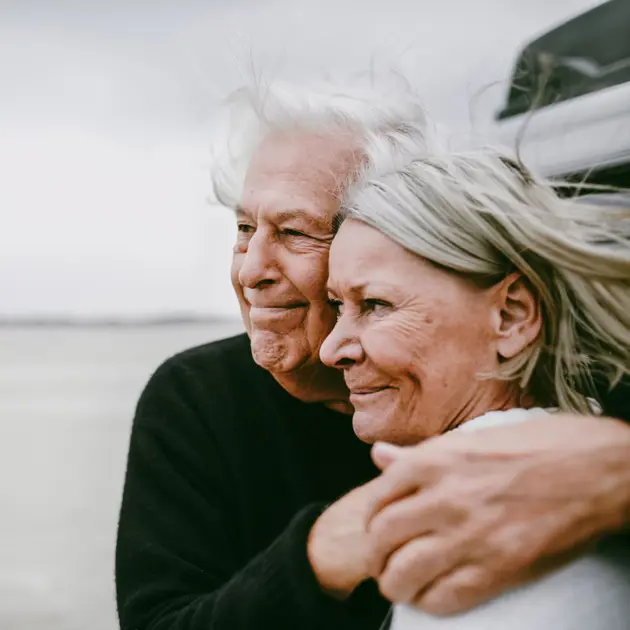 Två pensionärer kramas vid havet.