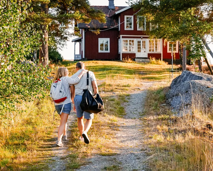 Par som promenerar mot en traditionell svensk röd stuga på landet en solig dag