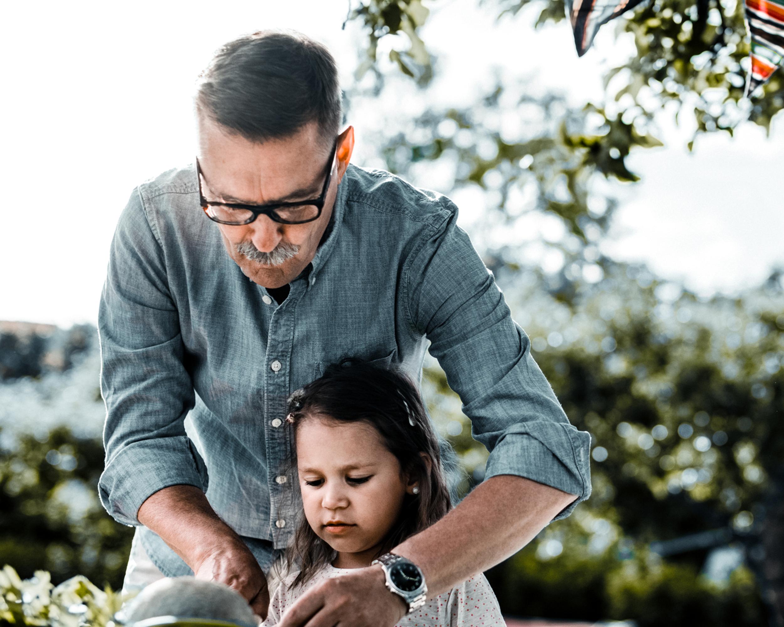 En pensionär med sitt barnbarn i en trädgård.