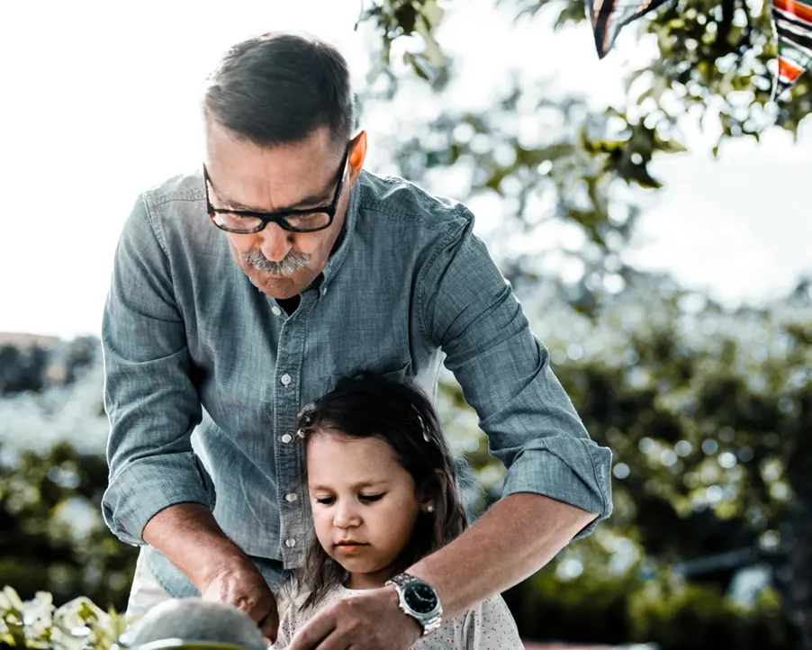 En pensionär med sitt barnbarn i en trädgård.