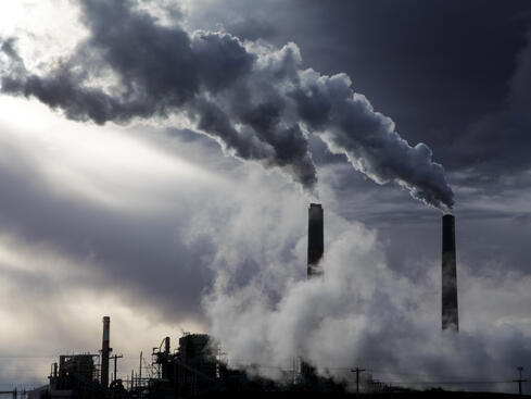 Industriskorstenar släpper ut tjock rök under en mörk himmel, symboliserar luftförorening och miljöpåverkan