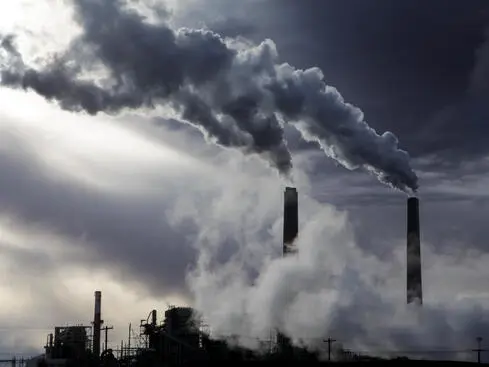 Industriskorstenar släpper ut tjock rök under en mörk himmel, symboliserar luftförorening och miljöpåverkan