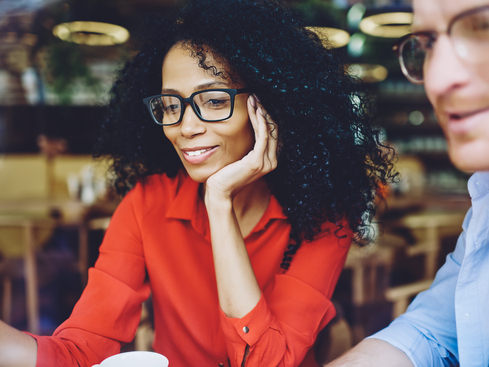 Kvinna i röd skjorta med glasögon i samtal med man på café