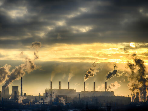 Industriell fabrik med r&#xF6;kstaplar som sl&#xE4;pper ut f&#xF6;roreningar under en dramatisk solnedg&#xE5;ng