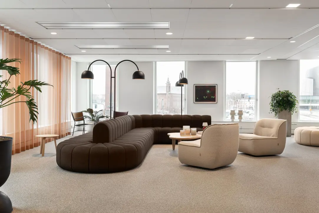 Modern och stilren kontorsmiljö med stora fönster, brun soffa, beige fåtöljer och gröna växter, skapar en inbjudande och avkopplande atmosfär