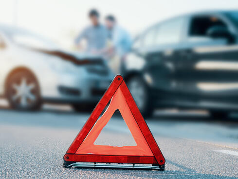 Varningstriangel på vägen med två bilar som har krockat i bakgrunden