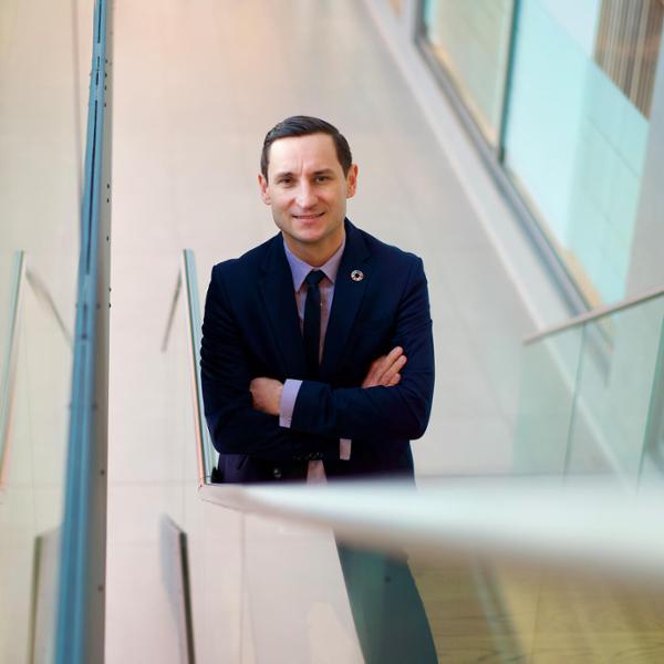 Man i kostym och slips står med armarna i kors i en ljus och modern byggnad