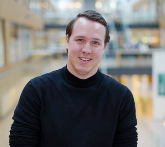 Man i svart tröja står i en modern byggnad med suddig bakgrund