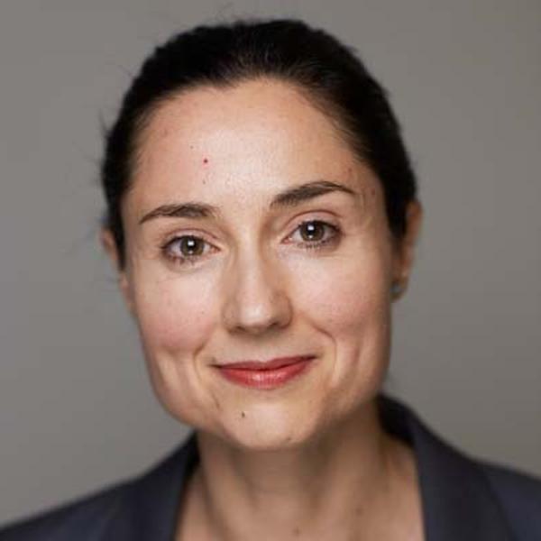 Porträtt av kvinna med mörkt hår och neutral bakgrund, iförd en mörk kavaj