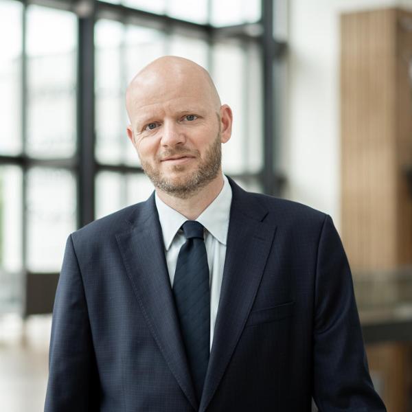 Man i kostym står i en ljus, modern kontorsmiljö och tittar in i kameran