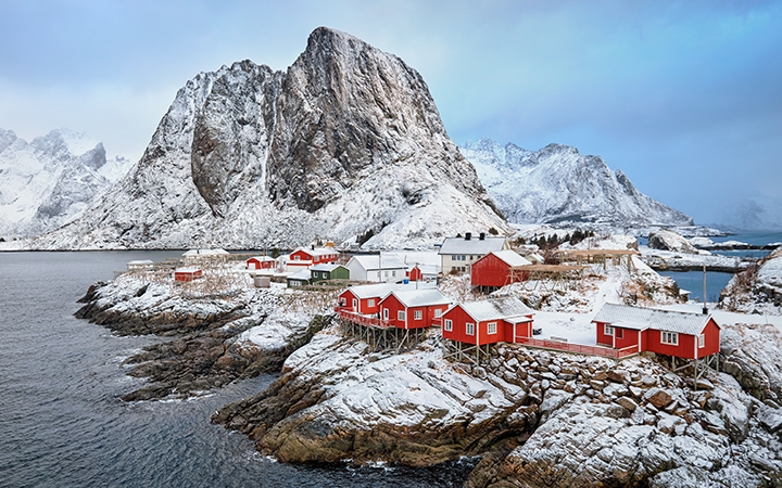 Vinterlandskap med röda stugor vid havet i Lofoten, Norge, omgiven av snötäckta berg och klippor