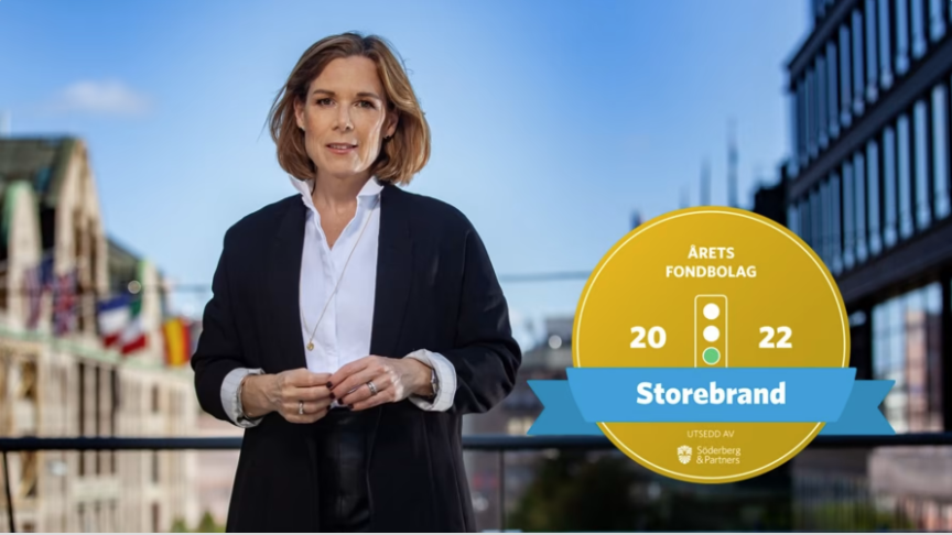 Kvinna står utomhus framför stadsmiljö, bredvid ett guldmärkt vinnaremblem för årets fondbolag 2022, Storebrand