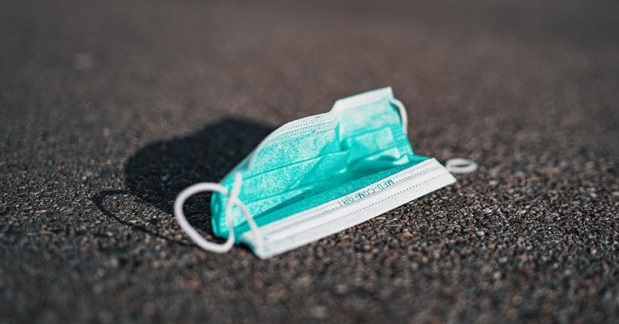Grön ansiktsmask ligger på asfalterad väg, symboliserar pandemins miljöpåverkan