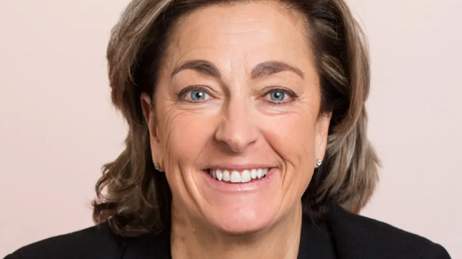 Leende kvinna med mörkbrunt hår och svart kavaj på ljus bakgrund