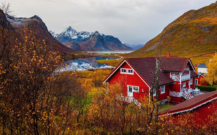 Röda hus i naturskön höstlandskap med berg och spegelblank sjö i Lofoten, Norge