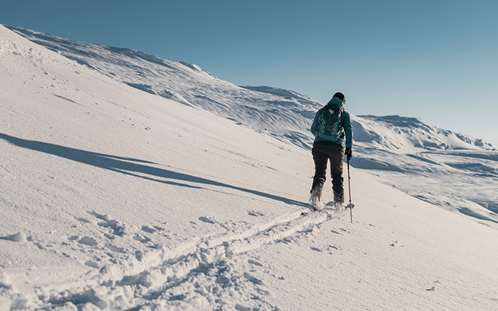 Person vandrar uppför snöig bergsluttning under en klar blå himmel