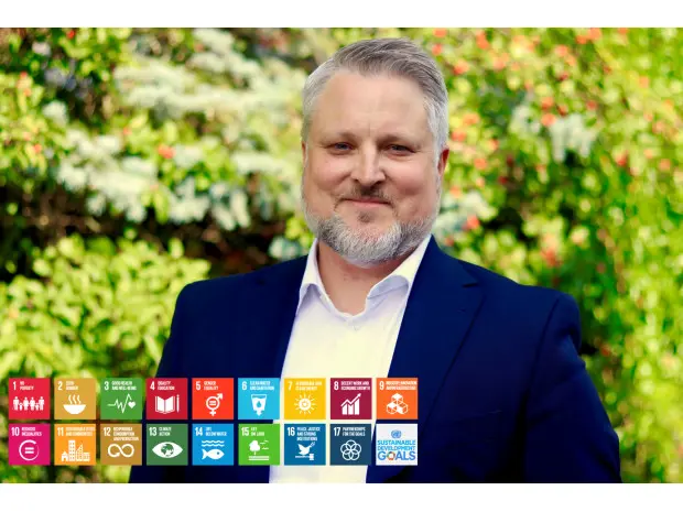 Man i kostym med hållbarhetsmålens symboler framför grönskande bakgrund