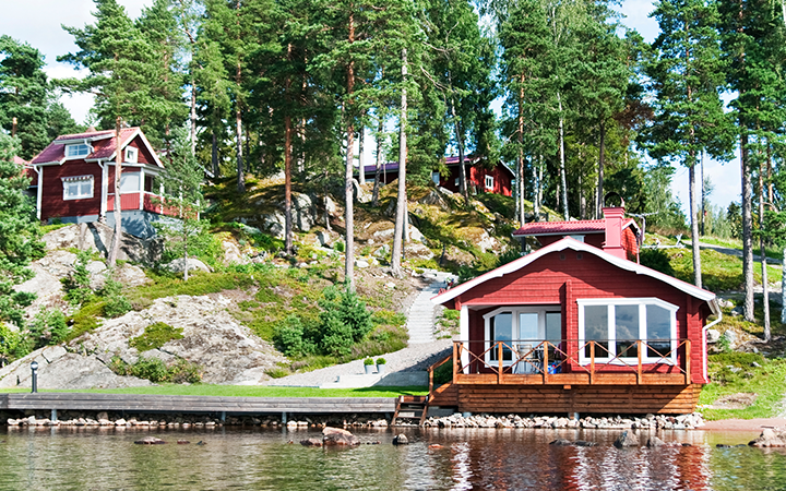Röd sommarstuga vid en sjö omgiven av tallskog, typisk svensk landsbygdsmiljö