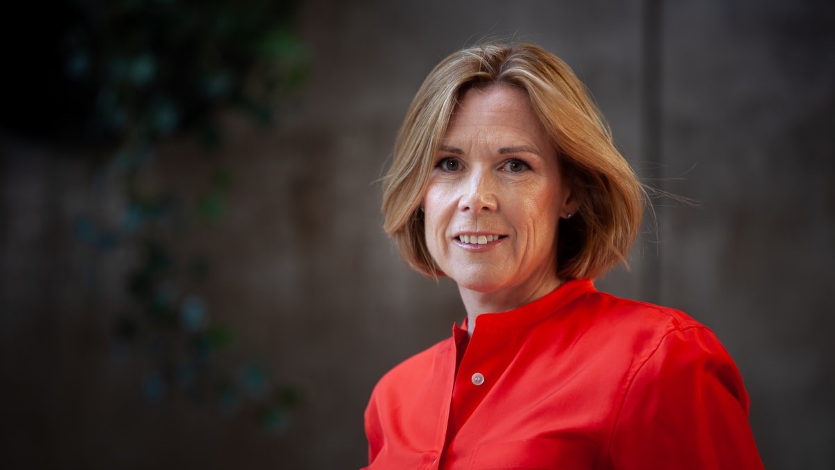 Kvinna i röd skjorta med kort hår står framför en suddig bakgrund