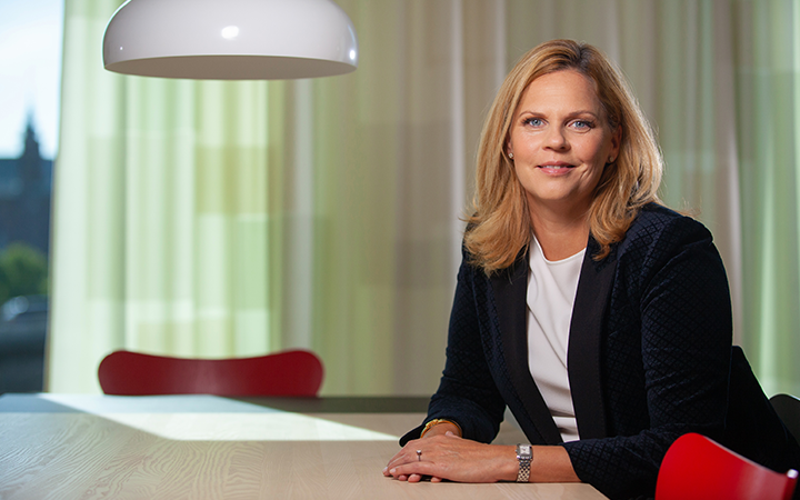 Kvinna i modernt kontorsmiljö vid ett bord med en lampa ovanför, röd stol i bakgrunden