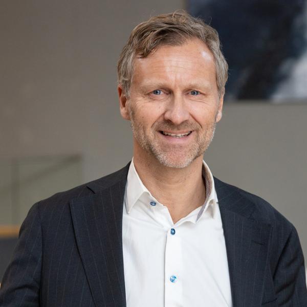 Man i kostym, ler mot kameran i en professionell miljö