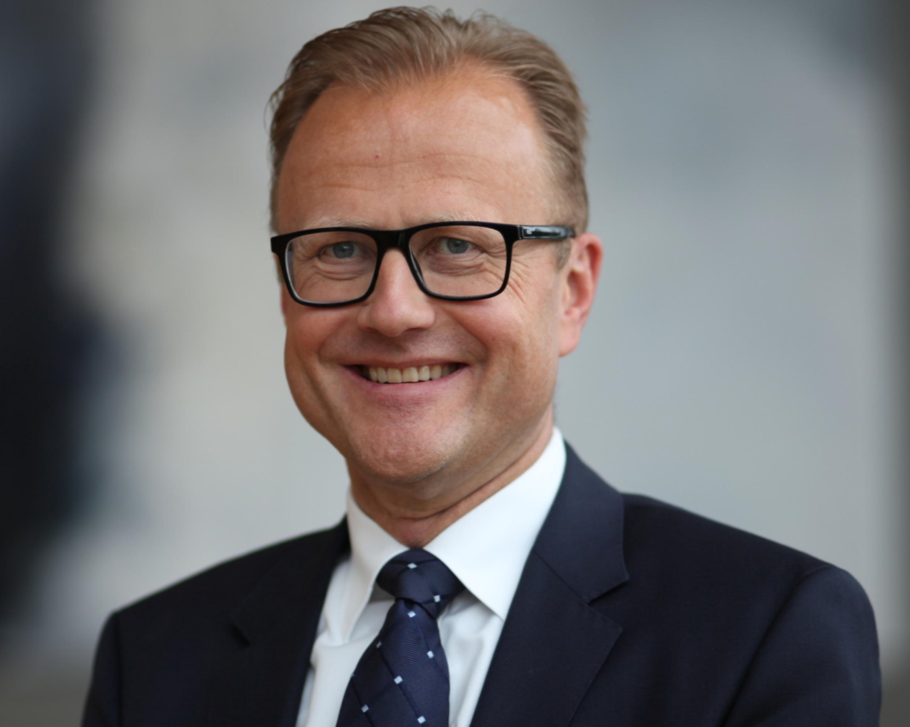 Man i kostym och glasögon ler framför en suddig bakgrund