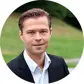Man i kostym med grönskande bakgrund utomhus