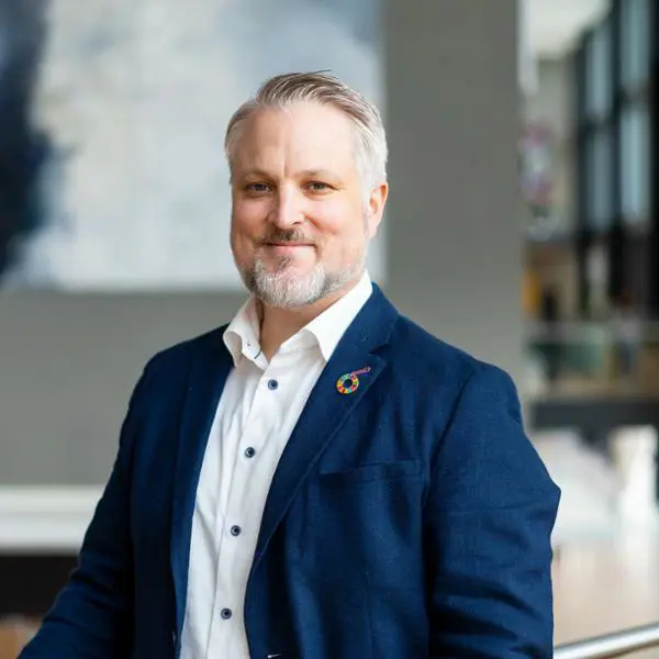 Man i blå kavaj och vit skjorta står i en modern kontorsmiljö